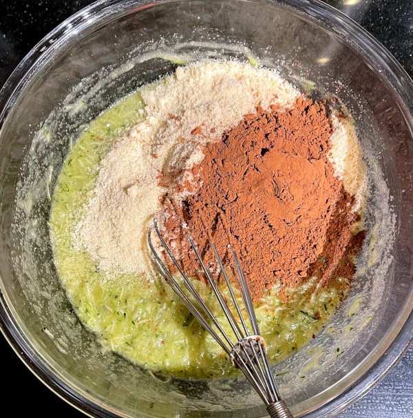 Grated zucchini in bowl with almond flour and cocoa powder.