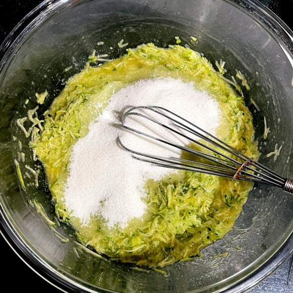 Erythritol added to grated zucchini and butter in bowl.
