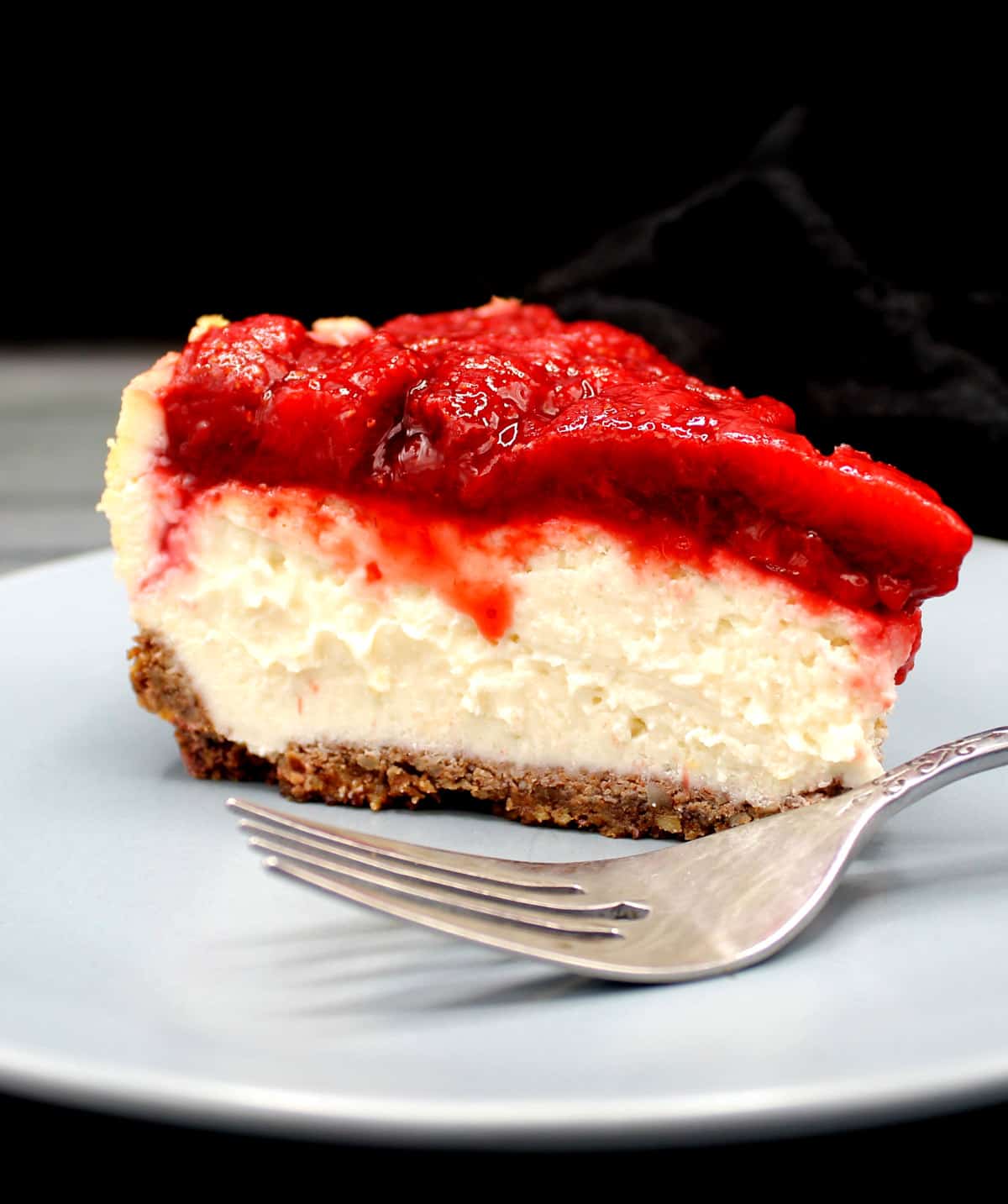 Side view of a creamy slice of vegan low carb cheesecake with strawberry topping.
