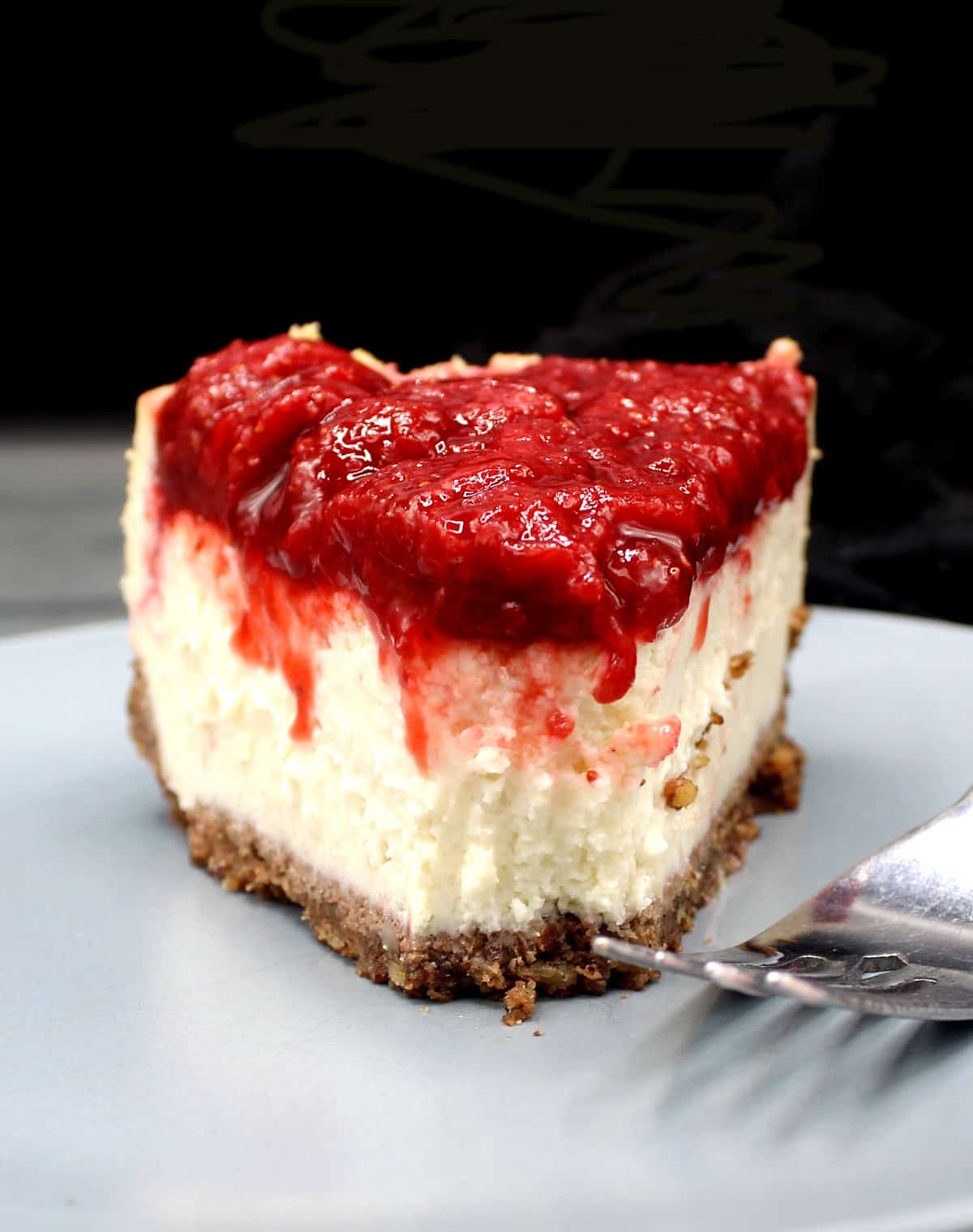 Slice of vegan keto cheesecake with strawberry topping and fork.