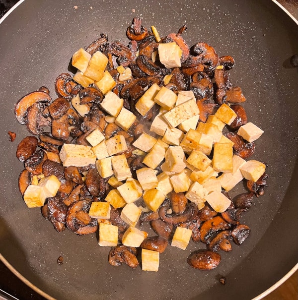 Tofu added to caramelized mushrooms in wok.