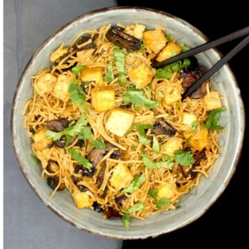 Overhead photo of vegan soba noodles in a bowl with mushrooms, tofu and cilantro and a pair of black chopsticks.