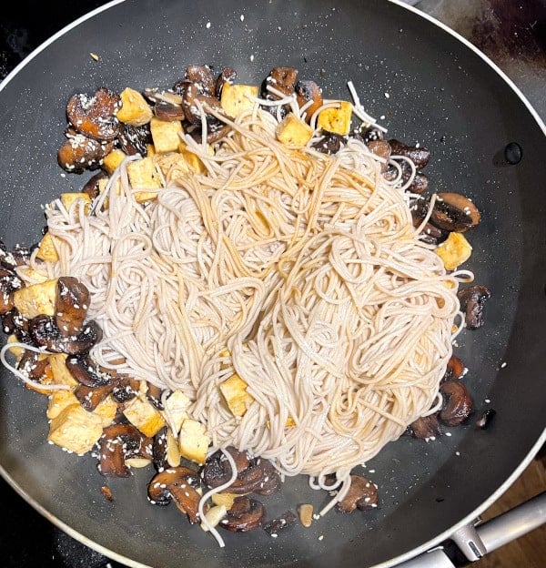 Noodles added to other ingredients for vegan soba noodles in wok.