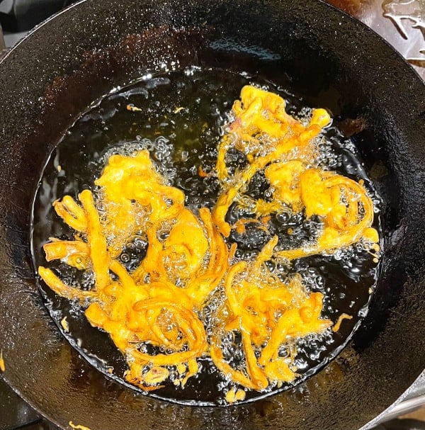 Onion pakoras frying in oil in kadhai.
