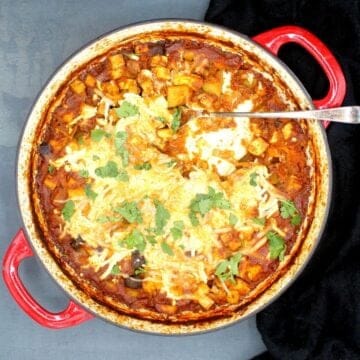 Overhead shot of a tofu casserole with vegan mozzarella cheese in a red and white braiser.