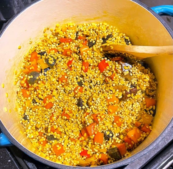Millets and moong dal stirred into vegetables in pot.