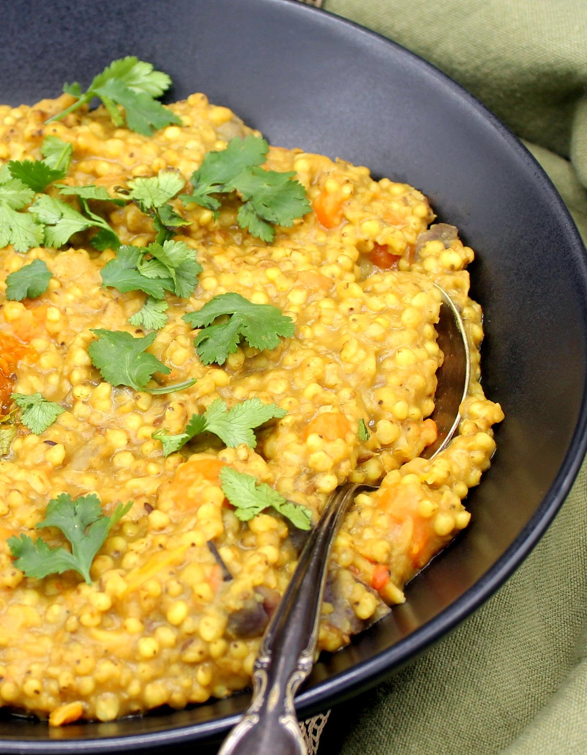 Front closeup photo of sorghum khichdi with cilantro in a black bowl.