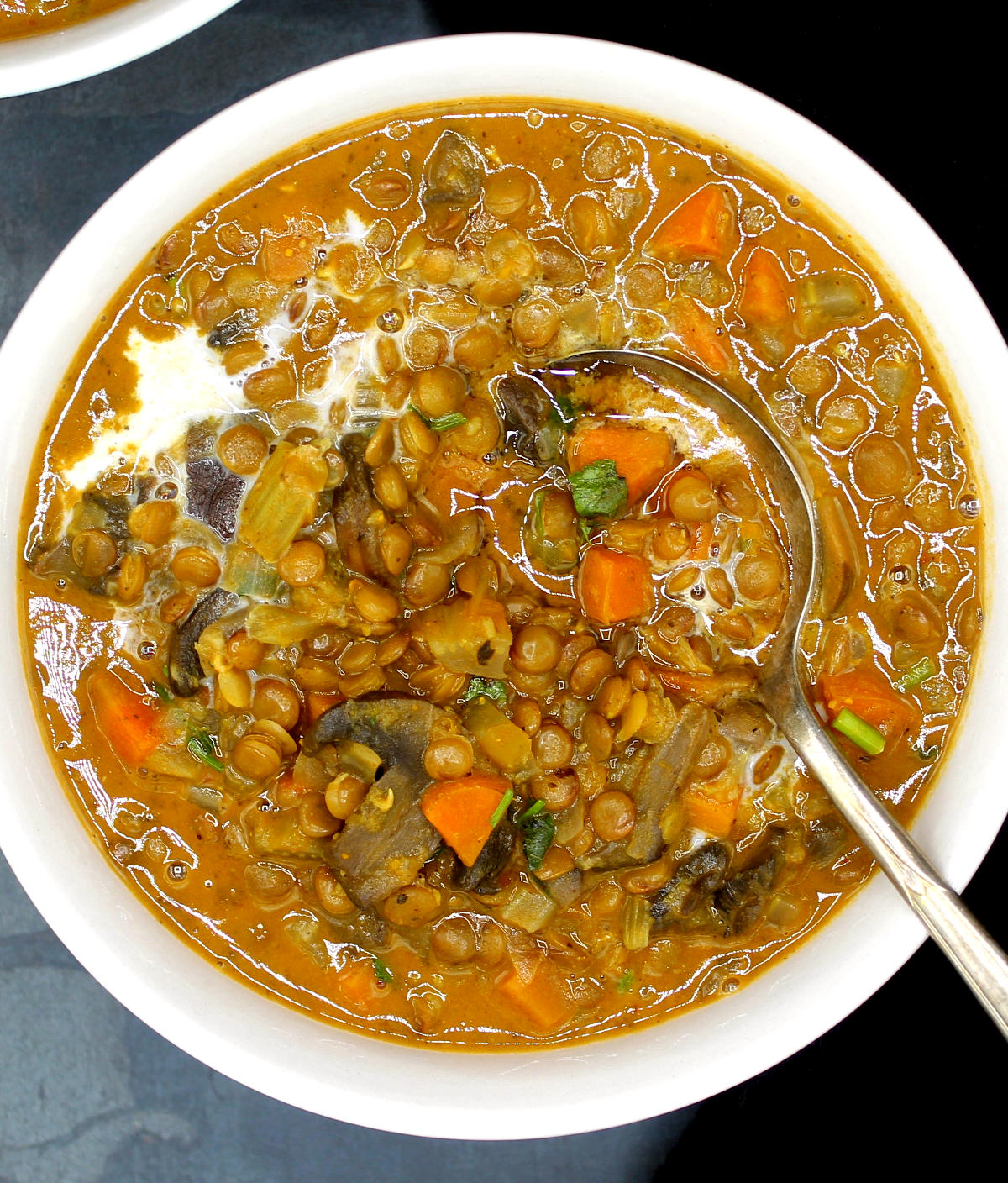 Brown lentil soup with vegetables and a spoon with coconut milk stirred in.