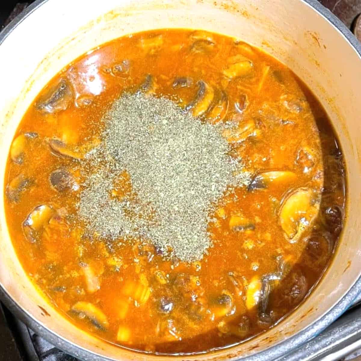 Dried mint added to lentil soup in pot.