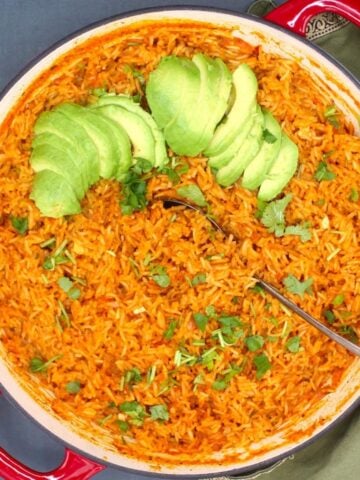 Mexican red rice with a garnish of cilantro and avocado in red and white skillet.