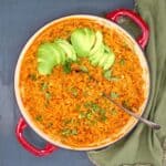 Mexican red rice in a skillet with avocado slices and cilantro and a spoon.