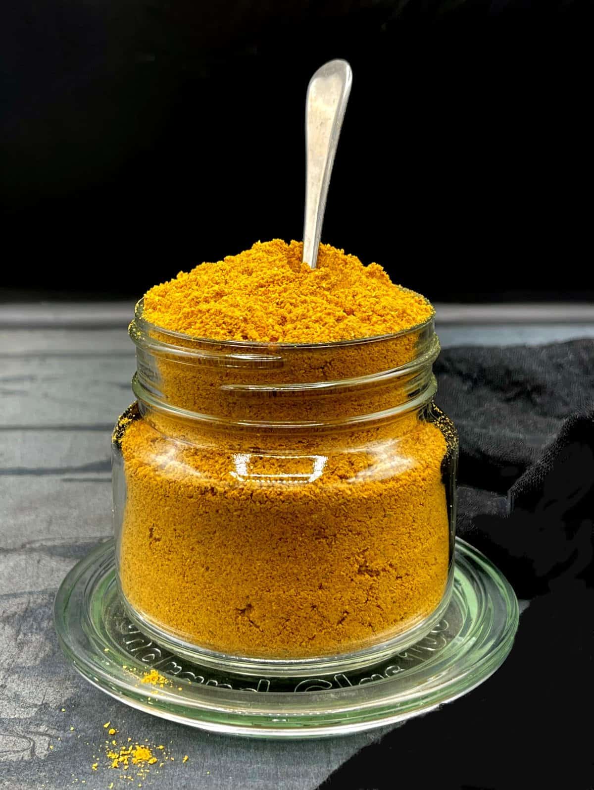 Front shot of a mason jar with sambar masala and a spoon in it.