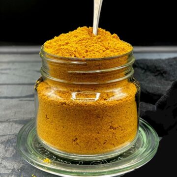Sambar powder filled to the brim in a mason jar with a spoon in it.