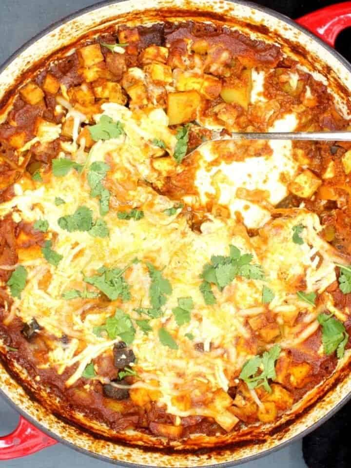 Vegan Indian spiced tofu casserole in red and white skillet with cheese on top.