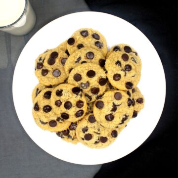 Overhead shot of a white plate with vegan keto chocolate chip cookies with a glass of almond milk in background.