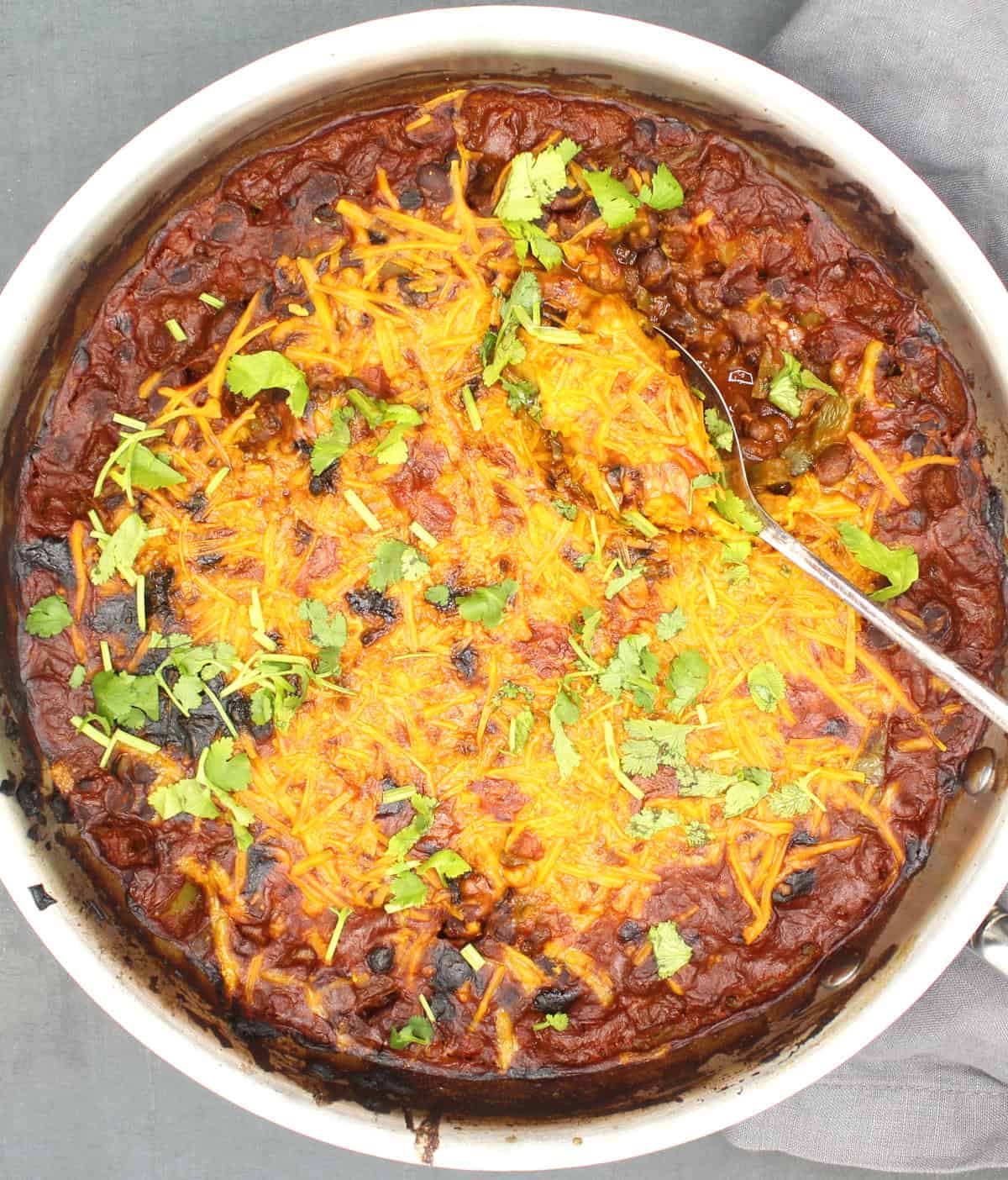 Mexican black bean casserole with cheesy topping and spoon.