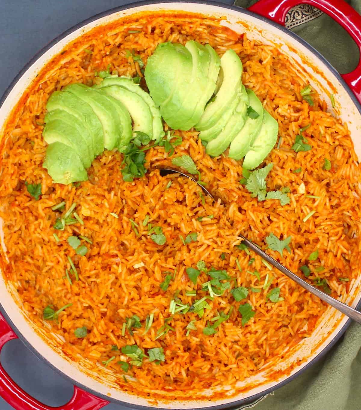 Overhead closeup of Mexican red rice in saute pan with cilantro and sliced avocado scattered over.
