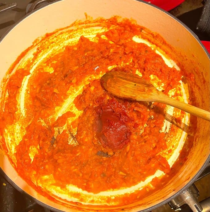 Tomato paste added to tomato puree in pan.