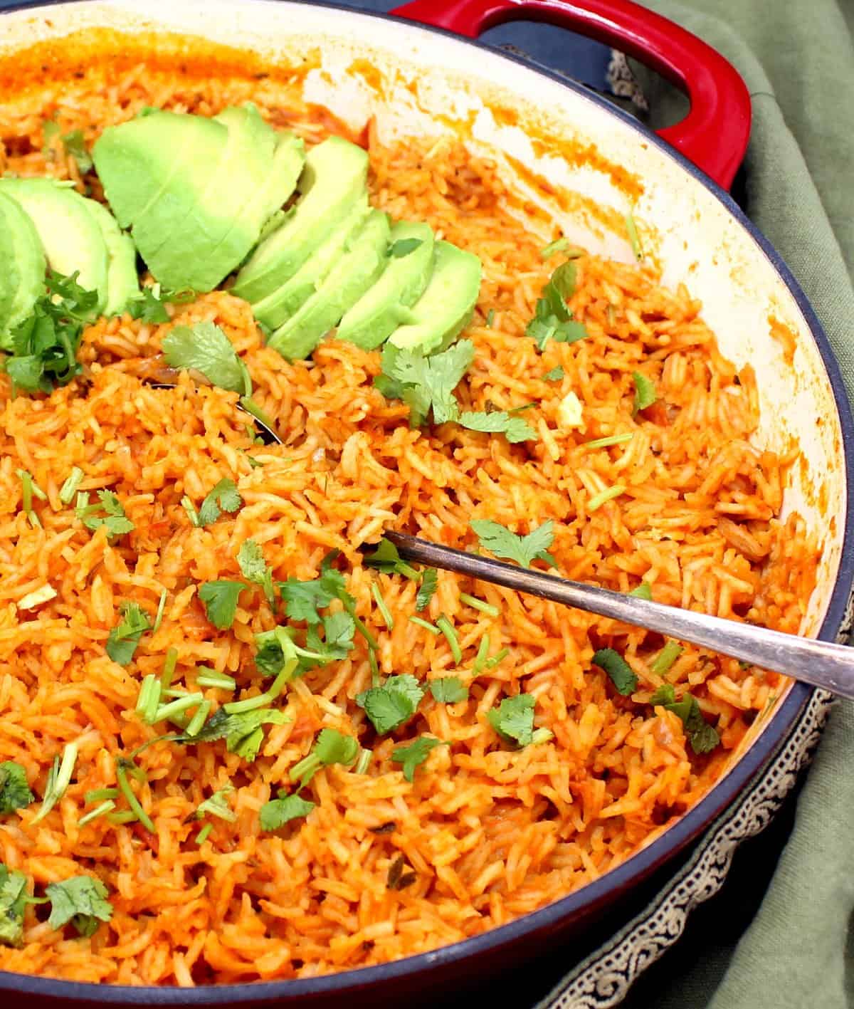 Front partial shot of Arroz Rojo, Mexican/Spanish red rice, with cilantro and avocado slices in saute pan.