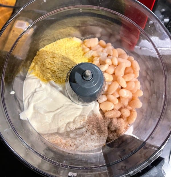 White beans, vegan yogurt and seasonings in food processor bowl.