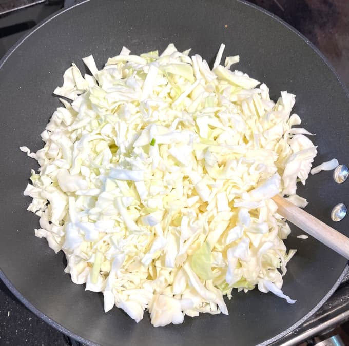 Cabbage added to wok with a wooden ladle in the wok.
