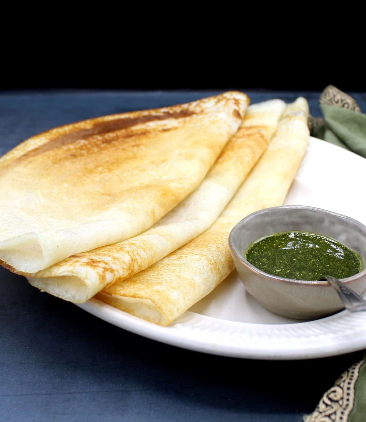 Front partial photo of three dosa on a plate with chutney in a bowl.