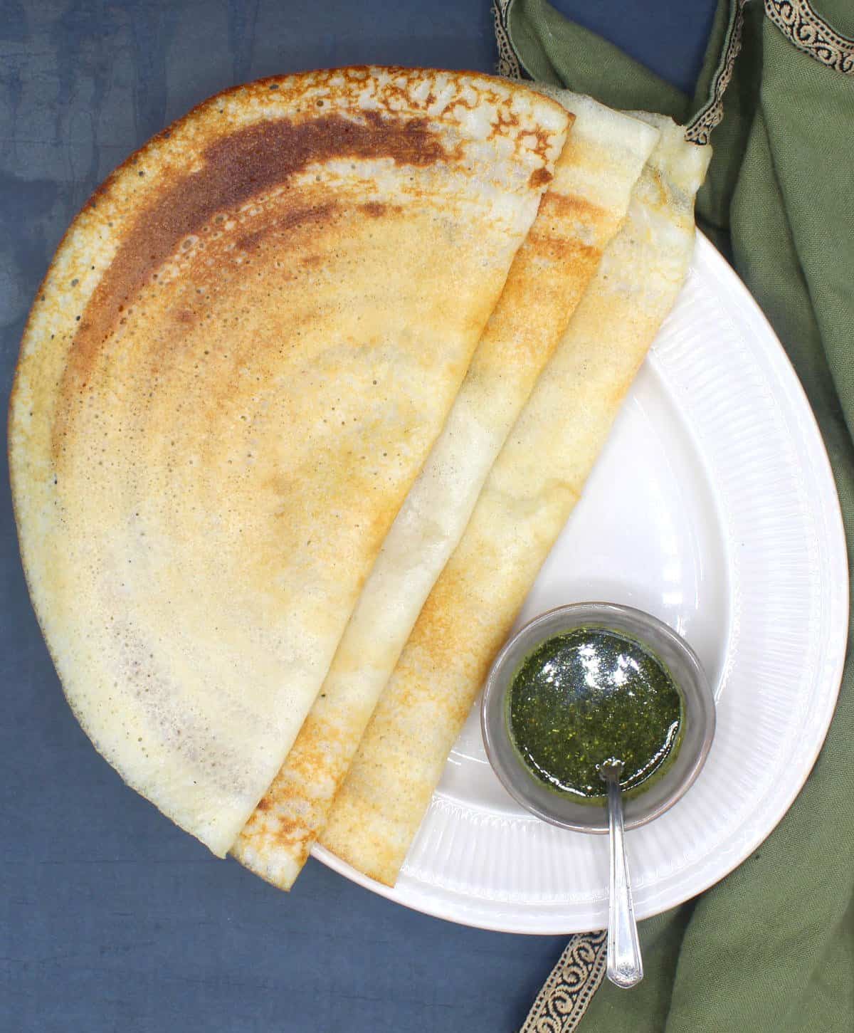 Overhead shot of three crispy dosas on a white plate with chutney in a small bowl.