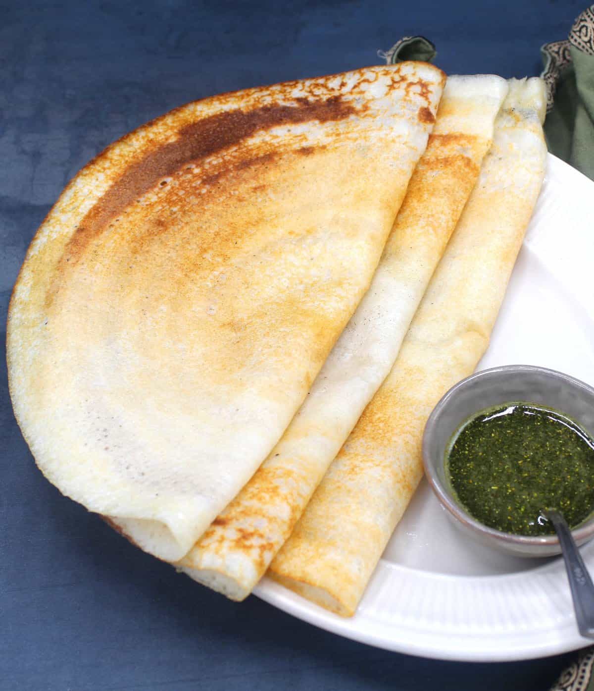 Front shot of three dosas on a white platter with chutney in a small bowl.