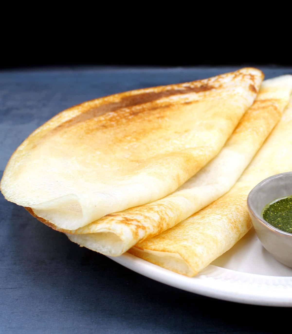 Front shot of three south Indian dosas on a plate with chutney.
