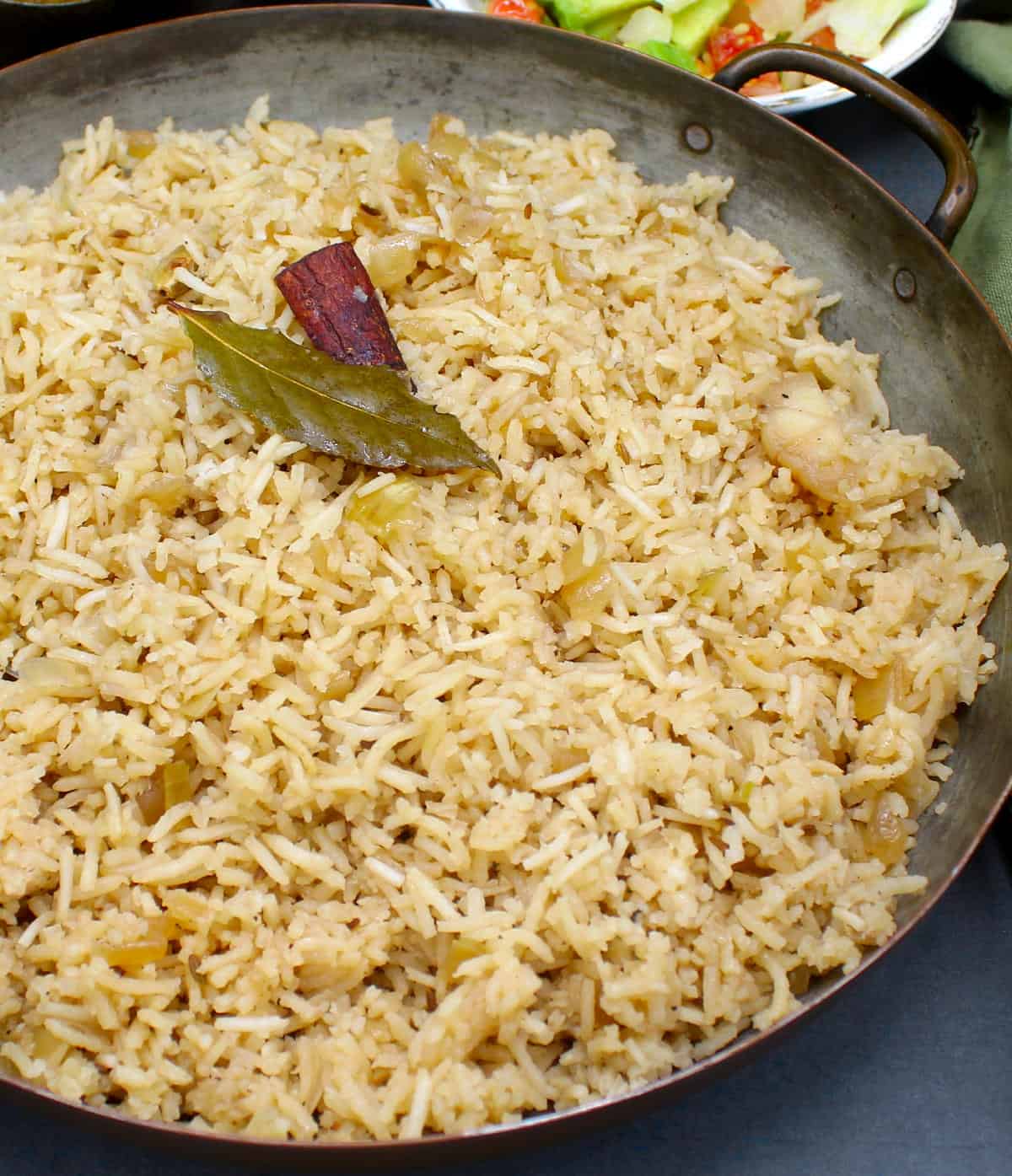 Parsi brown rice in a copper serving pan with a bay leaf and cinnamon stick.