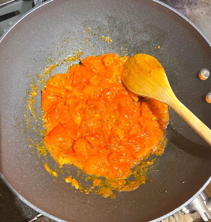 Tomatoes turned pulpy in wok with ladle.