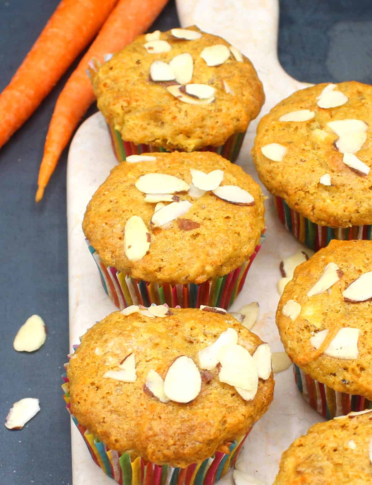 Front photo of six muffins on a marble serving board with almonds and carrots next to it.