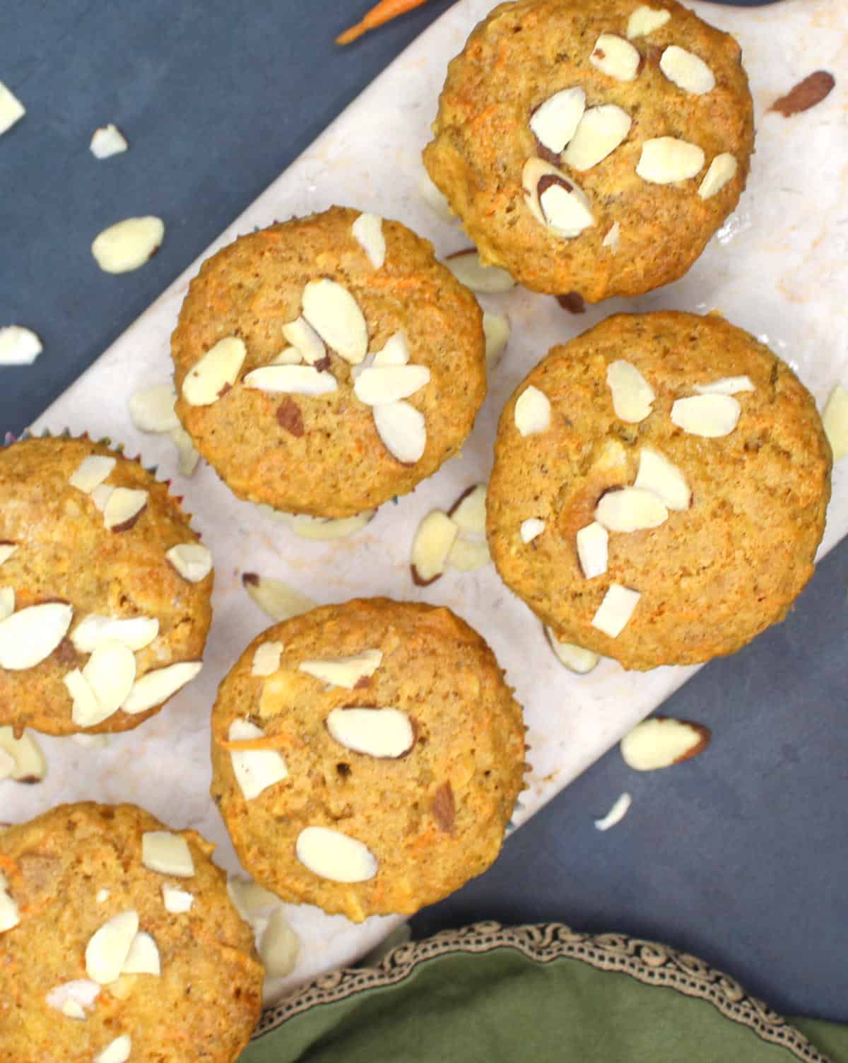 Overhead photo of vegan carrot muffins with almonds on a marble serving board with a green napkin on the side.