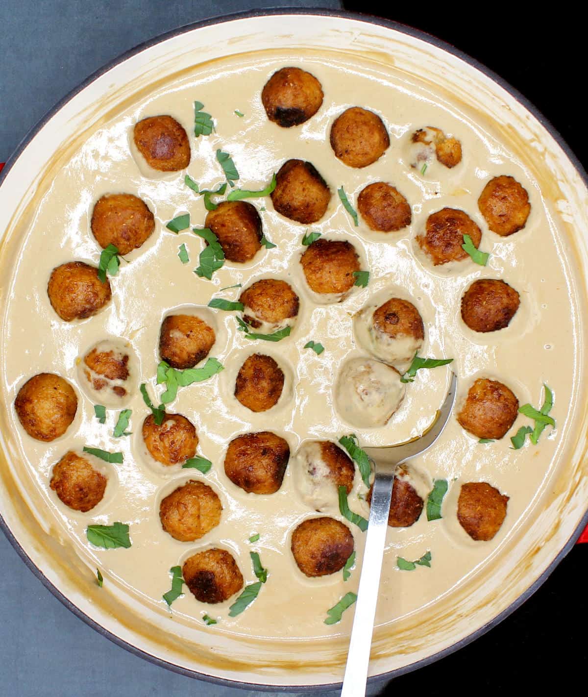Overhead photo of vegan meatballs in a cream sauce with ladle.