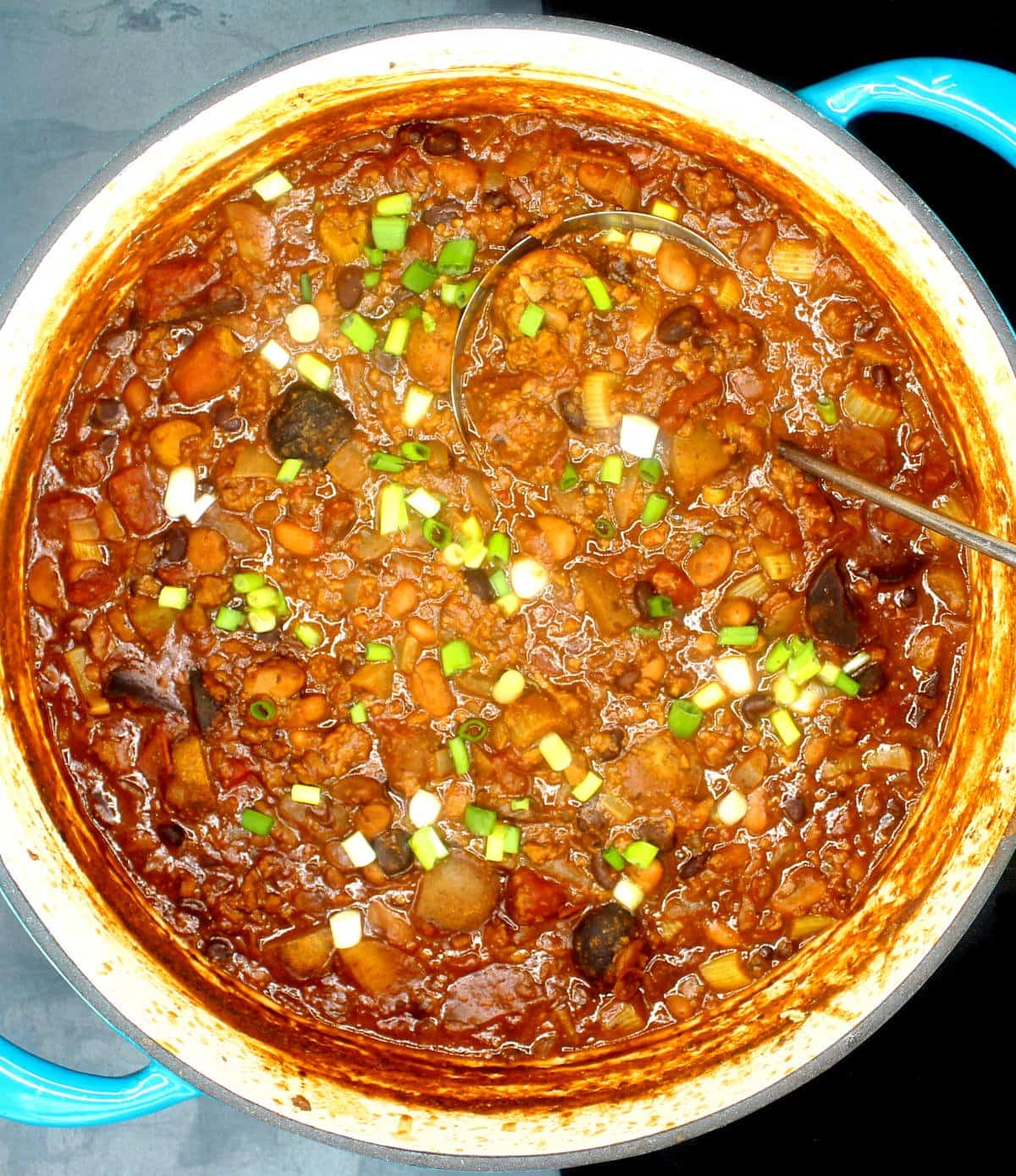 Overhead photo of a large pot of vegan Irish Chili with scallions and a ladle.