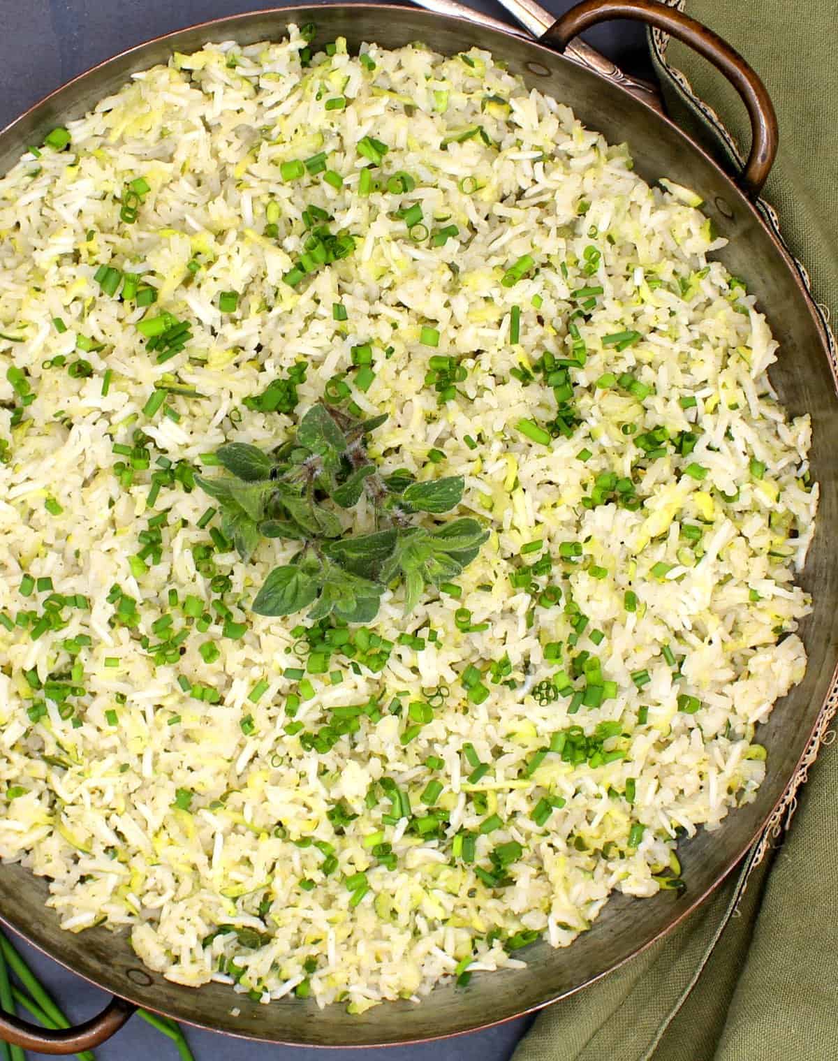 Overhead partial photo of a pot of vegan zucchini rice with chives, oregano and a green napkin next to it.