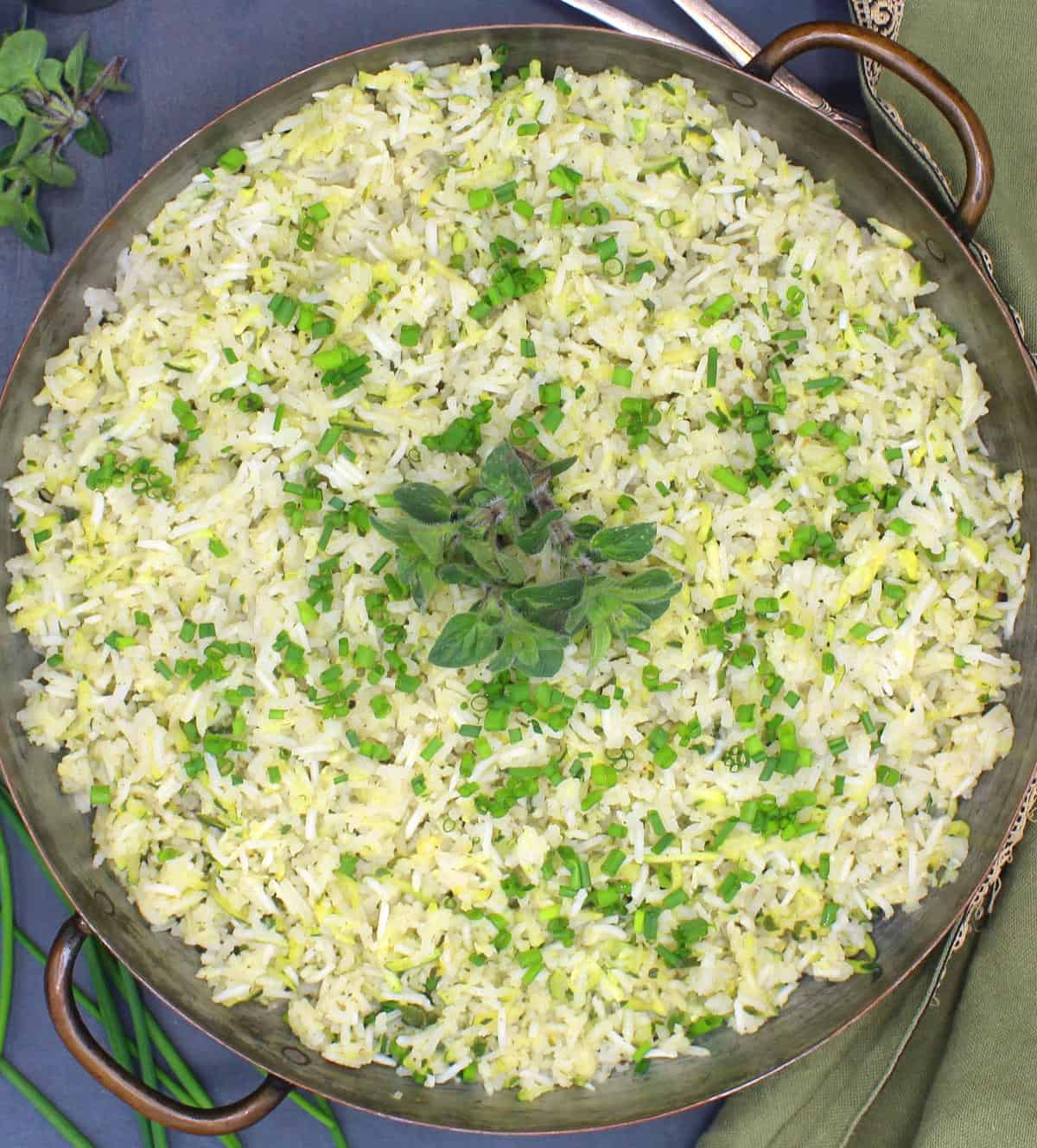 Overhead closeup photo of zucchini rice in a copper pan with chives and oregano.
