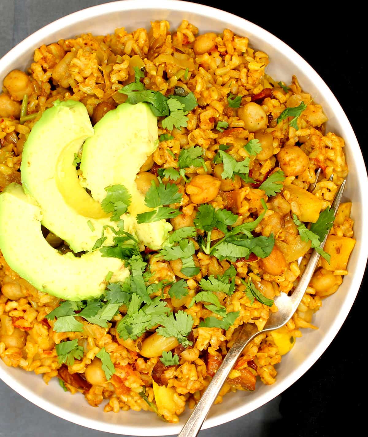 Overhead partial photo of a chickpea rice bowl with avocado, cilantro and a fork.