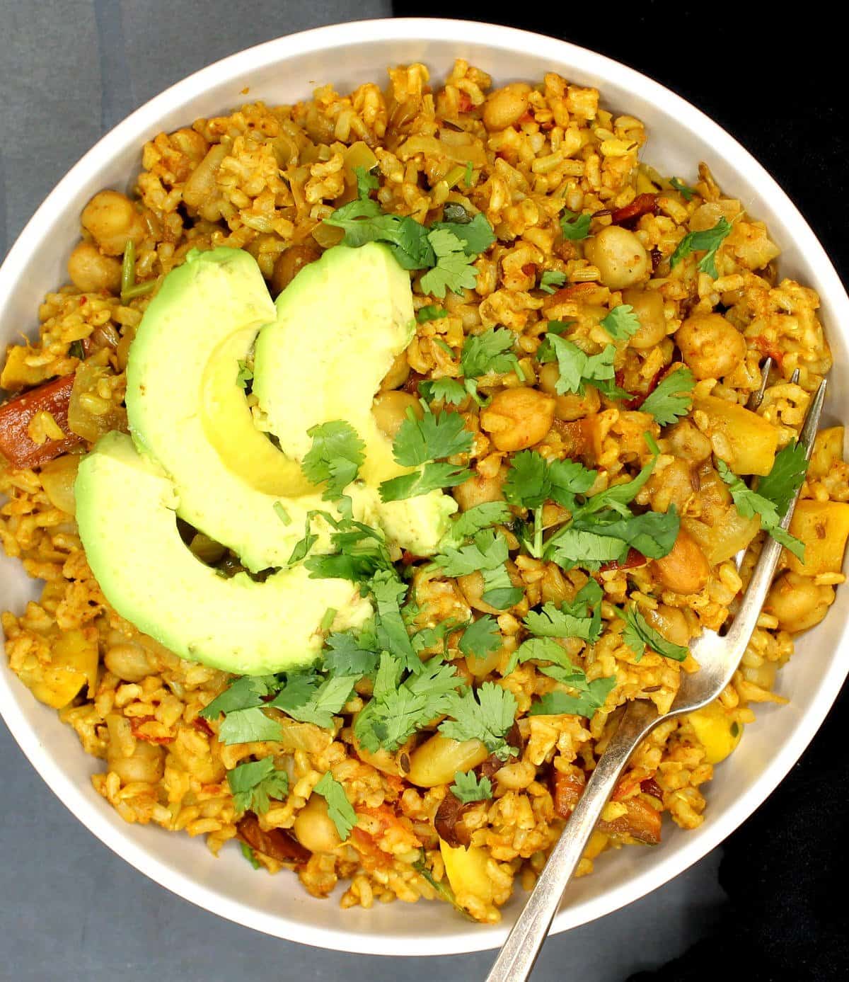 Overhead shot of chickpea rice bowl with avocado, cilantro and peanuts and a fork in the bowl.