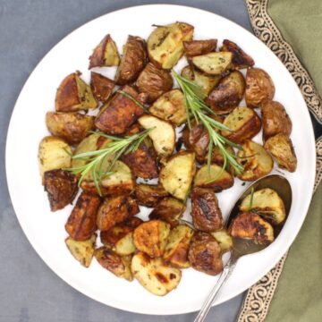 Rosemary roasted potatoes on a white plate with rosemary sprigs.