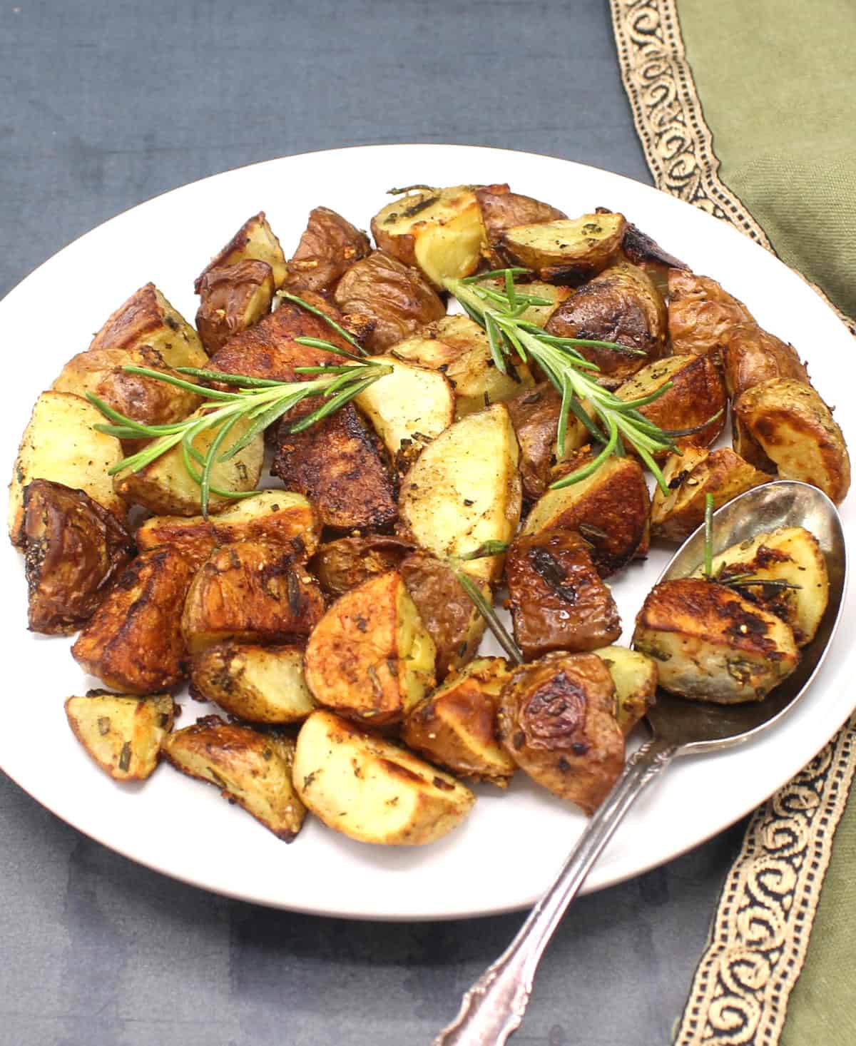 Rosemary roasted potatoes on plate with sprigs of rosemary and a spoon.