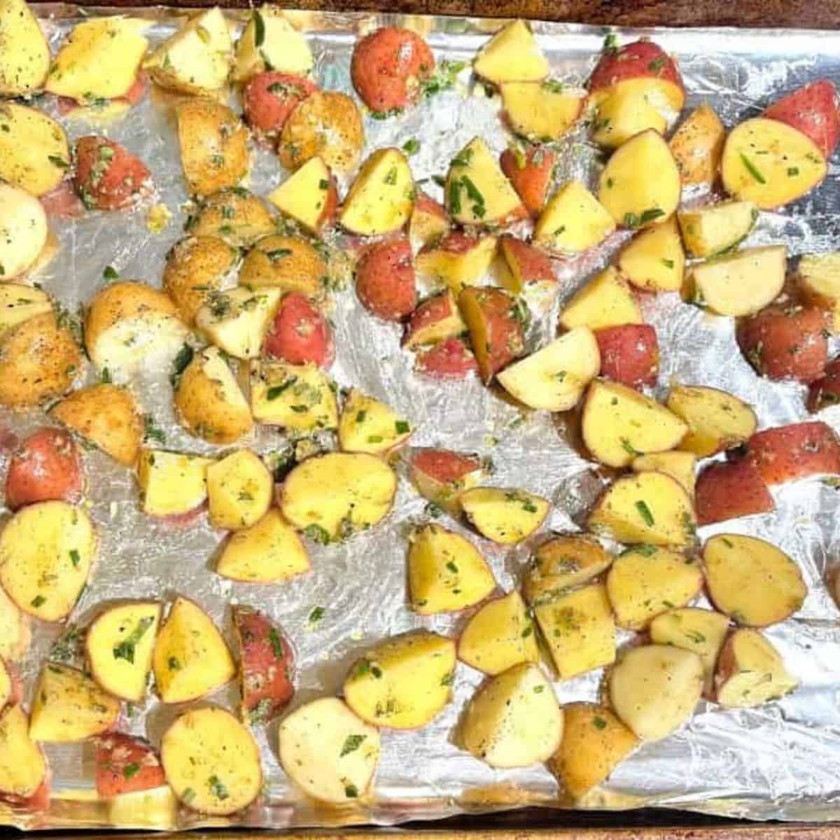 Potatoes mixed with rosemary marinade ingredients on baking sheet.