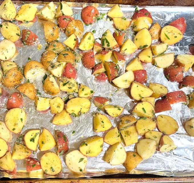 Marinated potatoes spread out on tinfoil lined baking sheet.