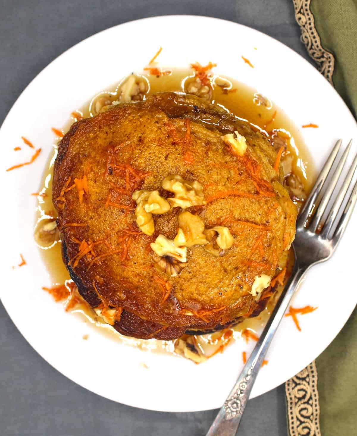 Overhead photo of vegan carrot pancakes in white plate with shredded carrots and walnuts and a fork.