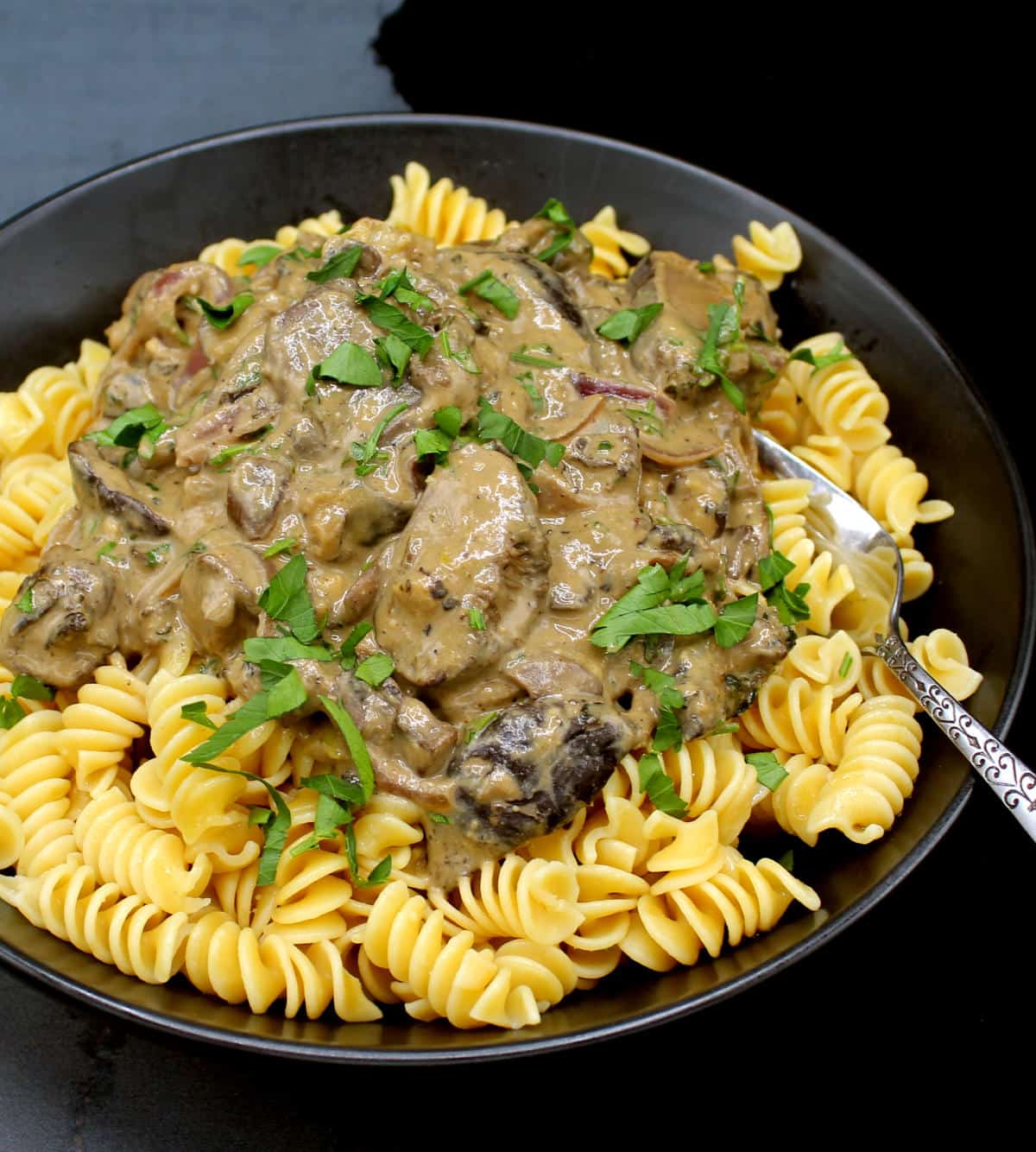 Front partial photo of mushroom stroganoff in black bowl with fork.