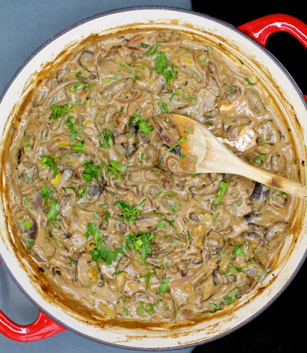 Overhead photo of vegan mushroom stroganoff in red and white skillet with wooden ladle.