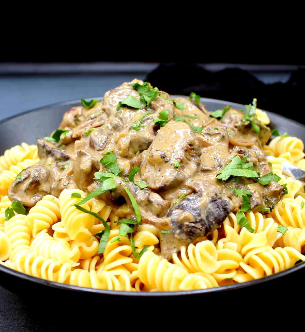 Front photo of vegan mushroom stroganoff in a black bowl with parsley.