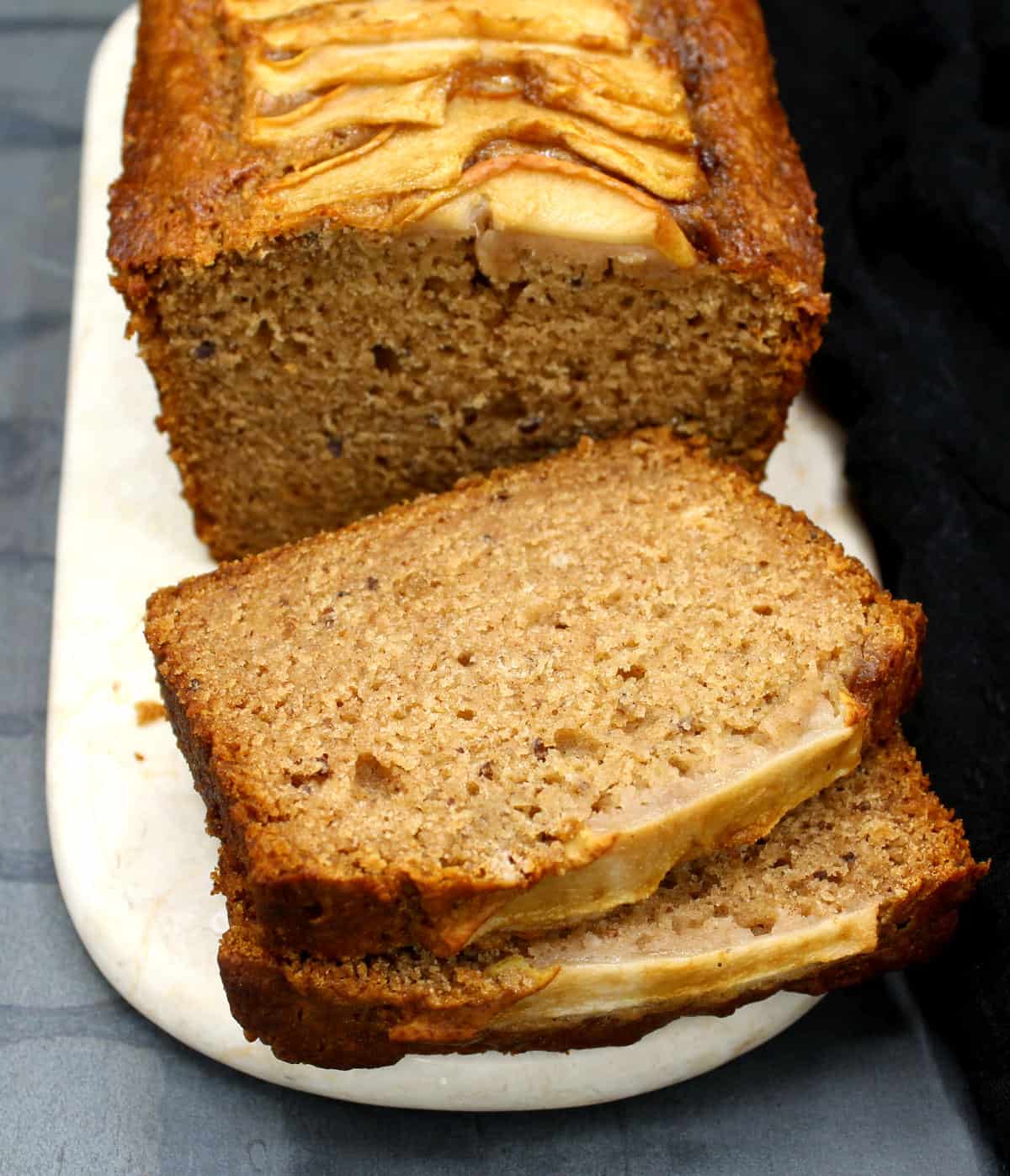 Sliced vegan pear bread with soft, moist crumb showing on a marble serving board.