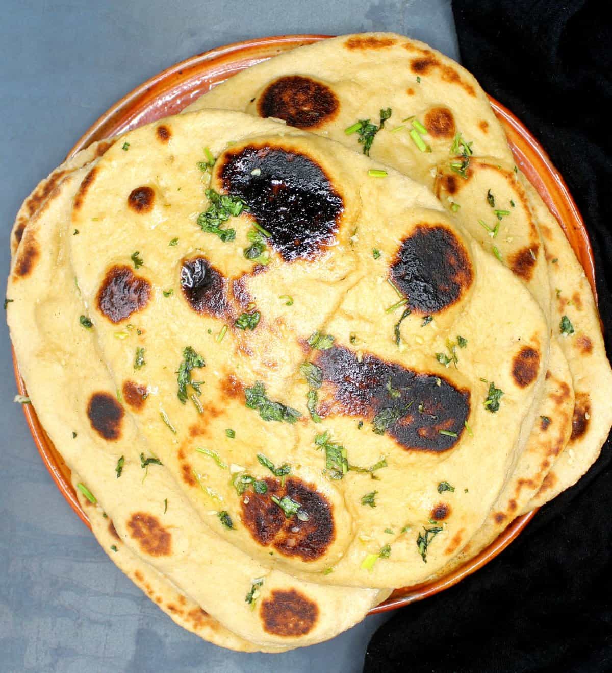 Overhead image of a stack of vegan whole wheat naans on a clay plate.