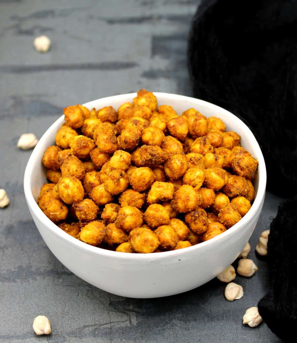 Crispy air fryer chickpeas piled in a gray bowl with chickpeas scattered around.